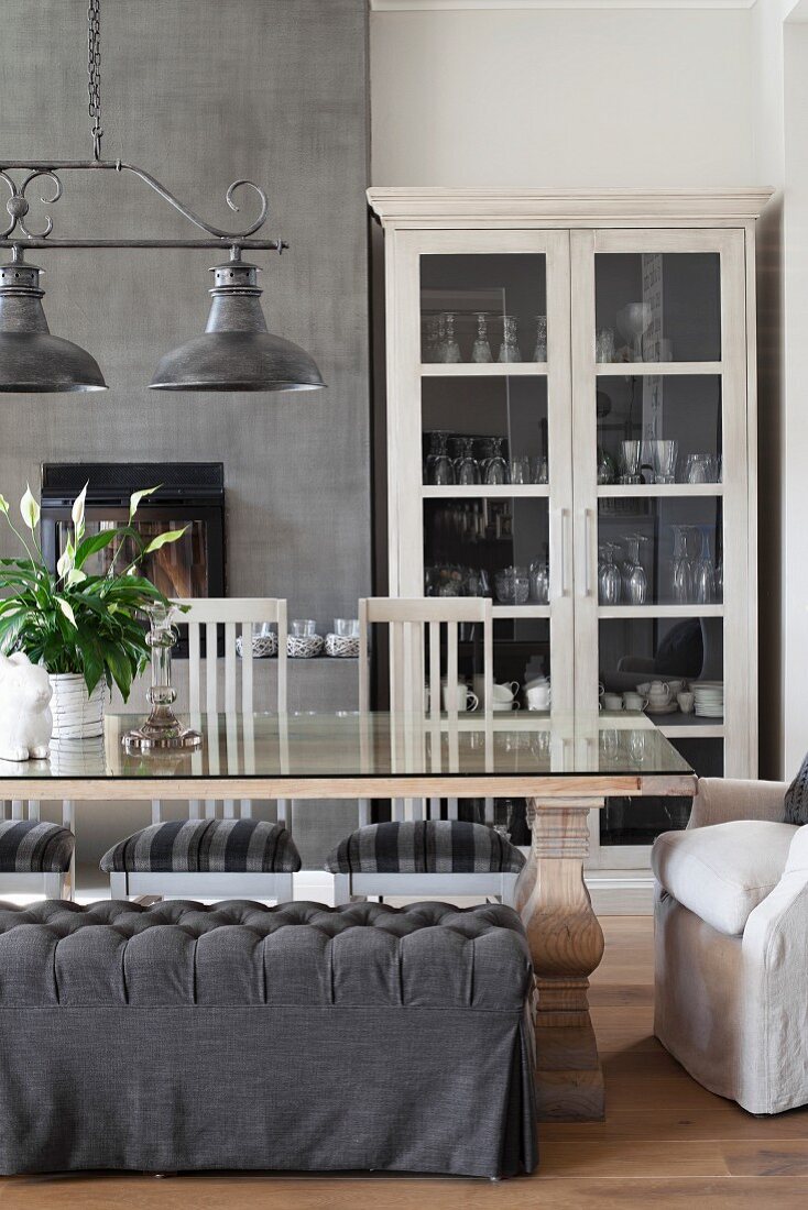 Bench with grey loose cover and white chairs around glass-topped table below vintage pendant lamps with metal lampshades