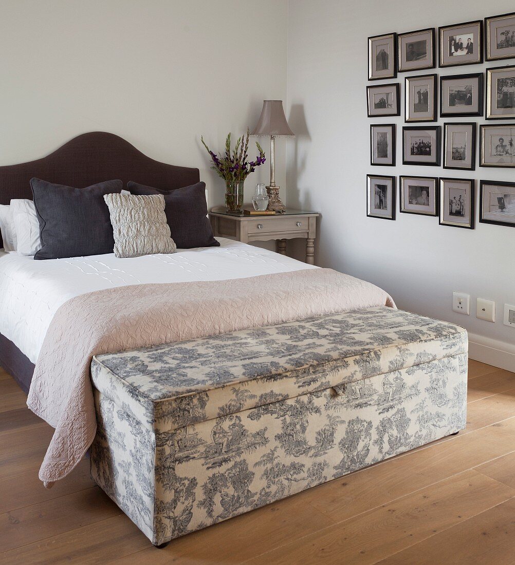 French bed with black, upholstered headboard and trunk upholstered in toile de jouy fabric at foot