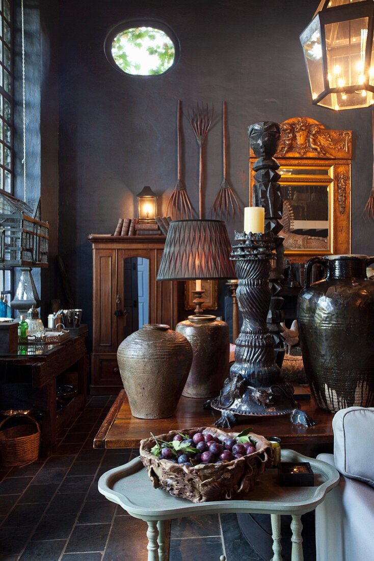 Freshly picked plums in basket on side table in front of antique, ethnic collectors' items on table in converted barn with black-painted walls