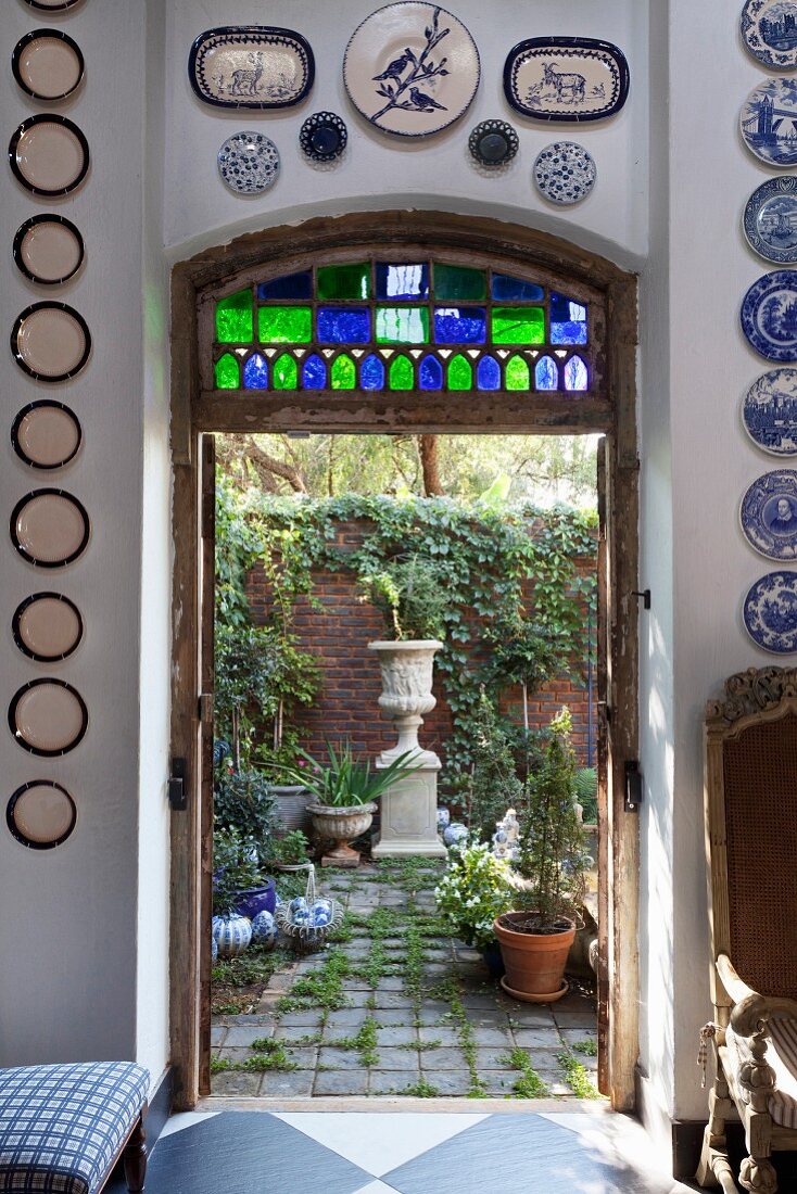 View through open door into planted back courtyard with urn and brick wall