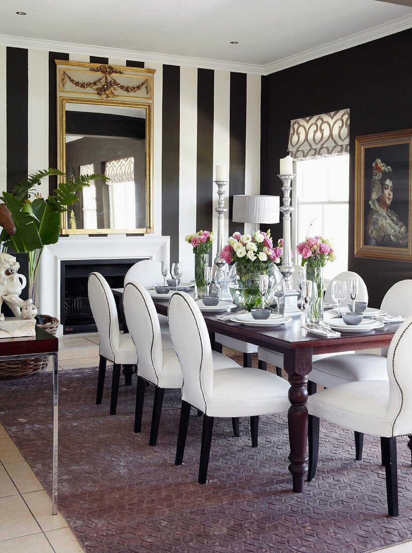 White, upholstered chairs and table in front of fireplace in dining room with black and white striped wallpaper