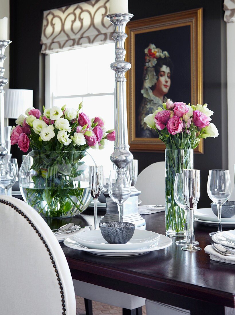 Festlich gedeckter Tisch mit Blumensträussen und Silber Kerzenhalter, im Hintergrund Gemälde an schwarzer Wand