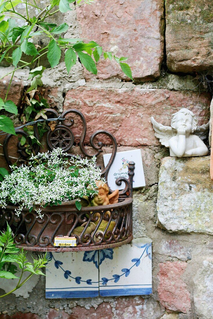 Rustic brick wall with cherub ornament and potted flowering plant in metal holder