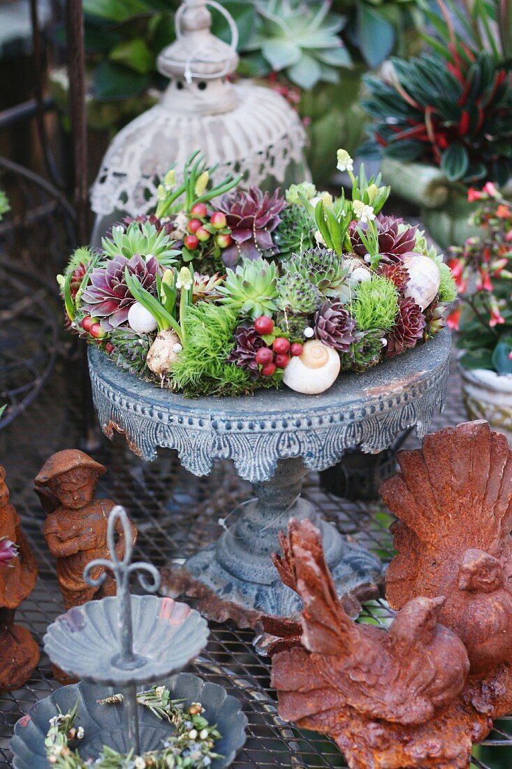 Decorative wreath of succulents with sempervivums on metal stand behind rust bird figurines