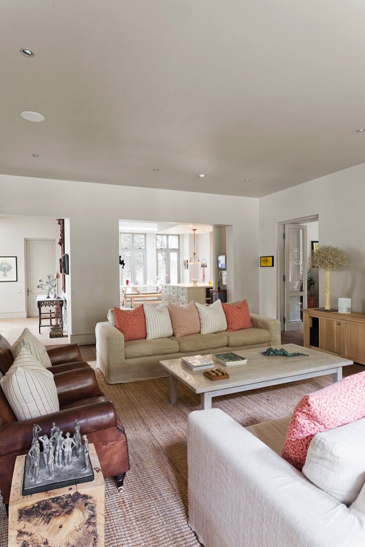 Comfortable living room with pale sofas, pastel scatter cushions and antique, brown leather armchairs