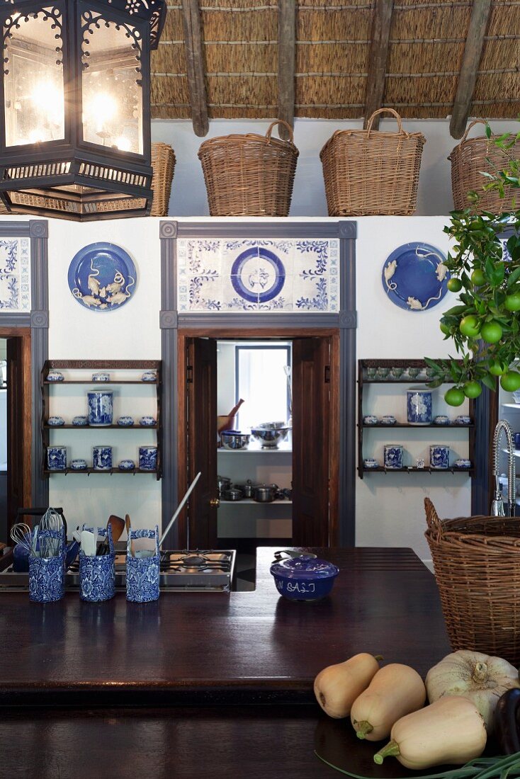 Kitchen counter in front of low installation with doors decorated with blue and white tiles and row of baskets on top