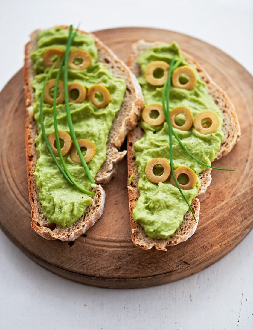 Slices of bread topped with avocado cream and green olives