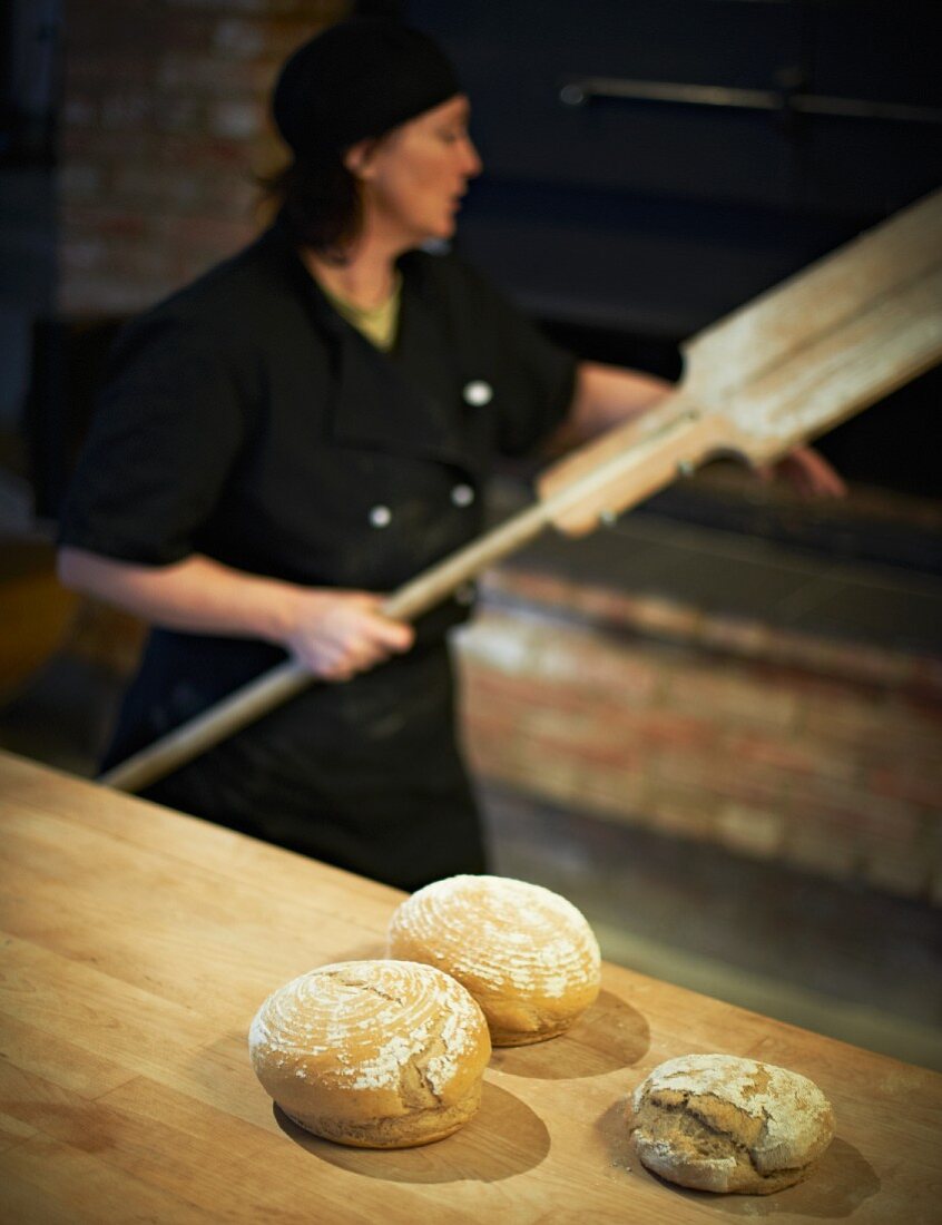 Bäckerin mit Broten vor dem Backofen