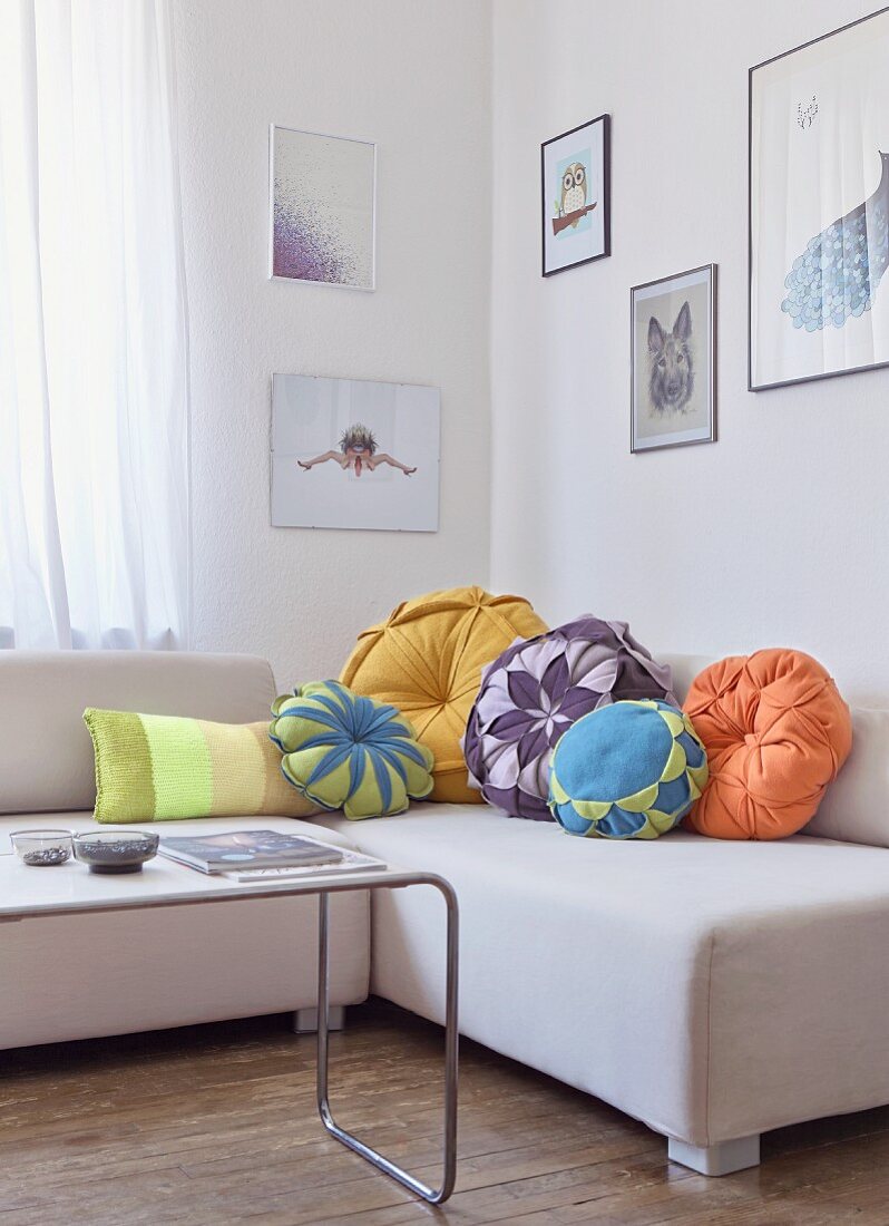 Various flower-shaped scatter cushions on pale, modern couch behind Thonet coffee table