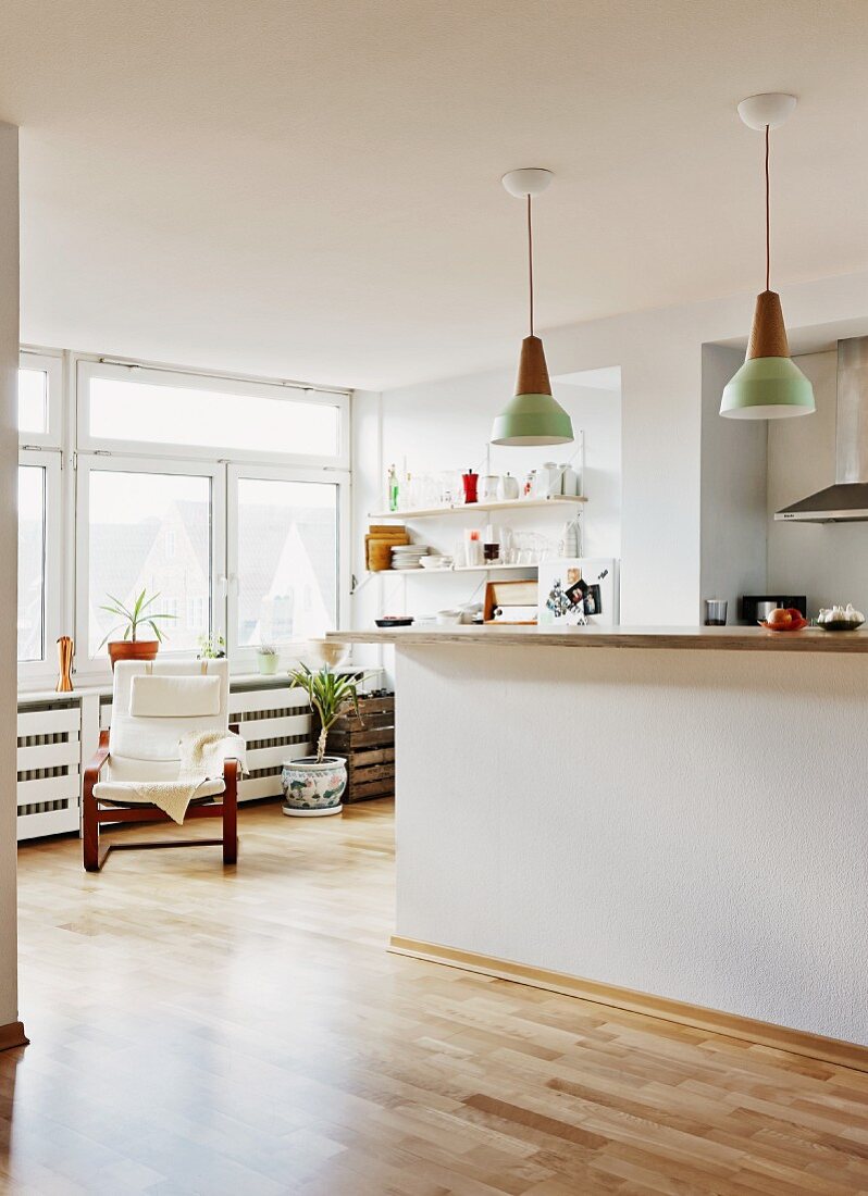 Küchentheke unter Retro Hängeleuchten in offenem Wohnraum, Sessel vor Fenster in reduziertem Ambiente