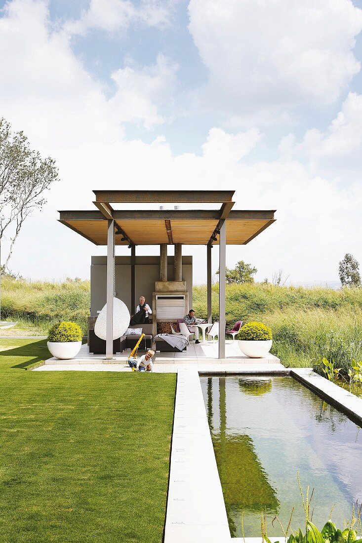 Pond and steel girder gazebo in landscaped garden surrounded by wild countryside