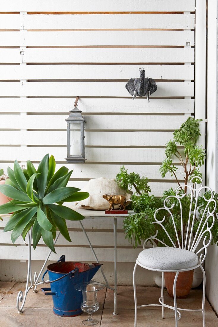 Delicate metal chair and table and planters against white wooden screen