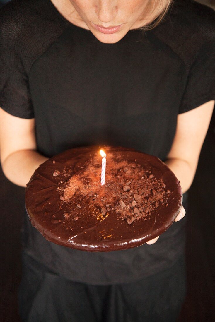 A woman holding a chocolate cake decorated with a candle