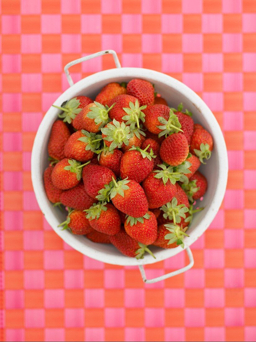Fresh strawberries in a colander on a checked surface