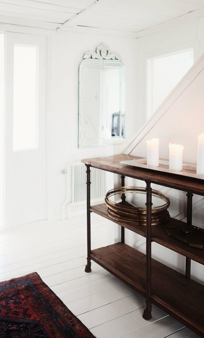 Kerzen auf hablhohem Regal aus dunklem Holz vor Treppenaufgang, in weißem, holzverkleidetem Hauseingang