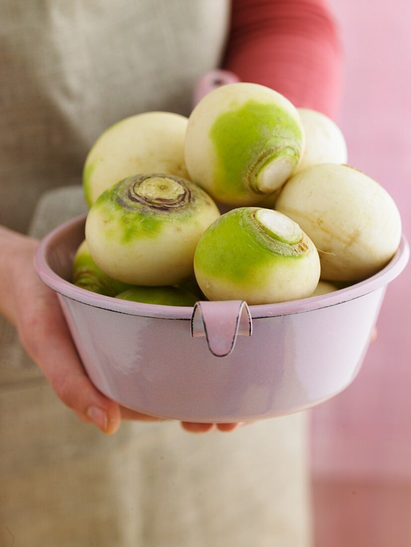 Hands holding a sieve filled with white turnips