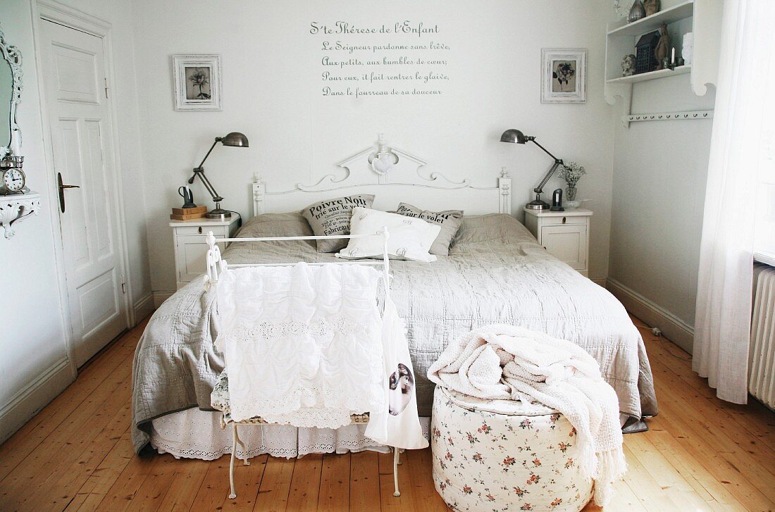 Valet stand and pouffe at foot of double bed with carved wooden headboard painted white in master bedroom