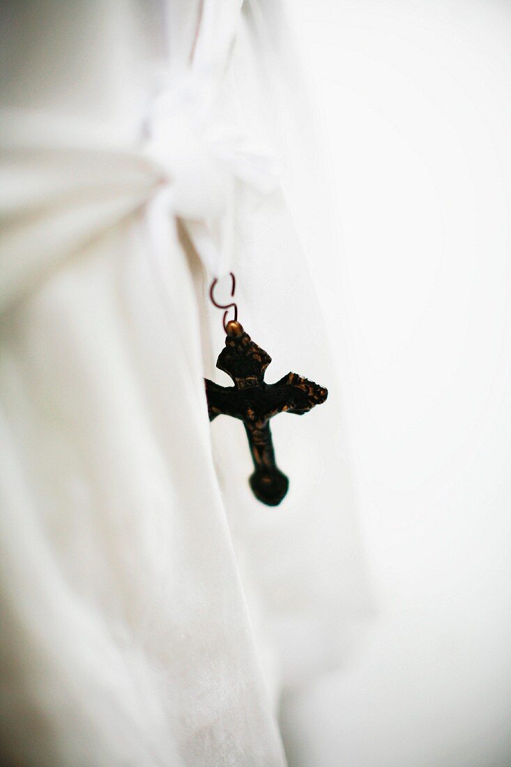 Vintage metal cross hanging from tie of loose chair cover