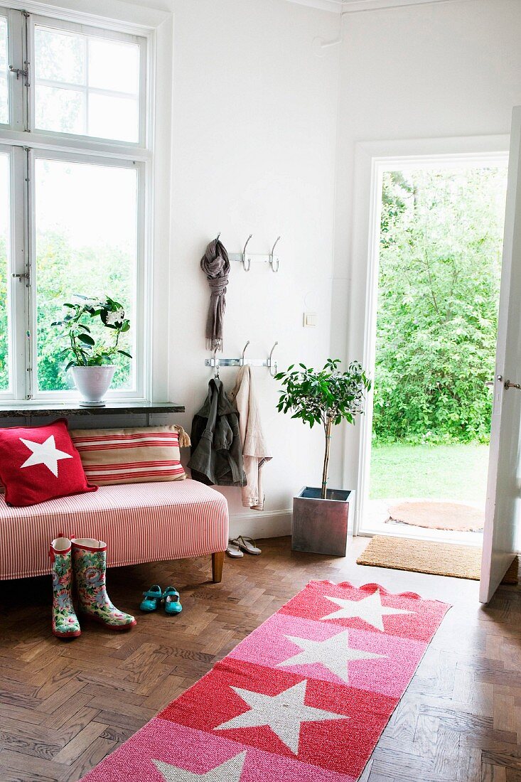Red and pink striped rug with star motif in comfortable interior with view of summery garden seen through open exterior door