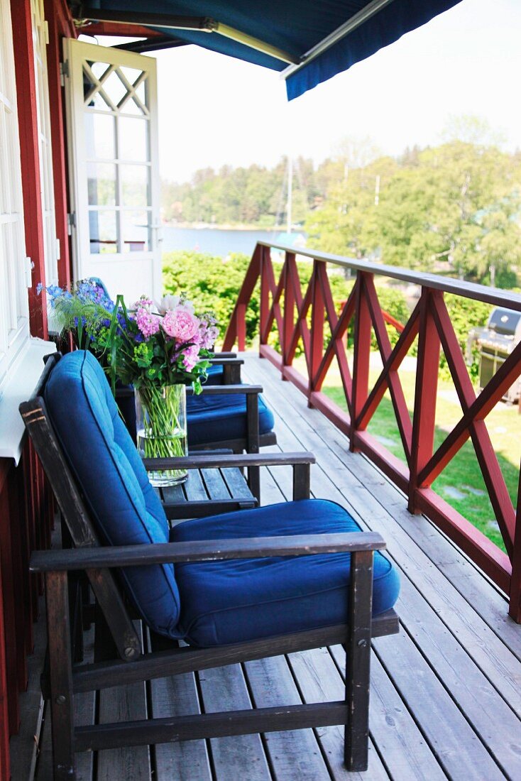 Dark garden furniture with blue cushions on wooden veranda adjoining Swedish wooden house