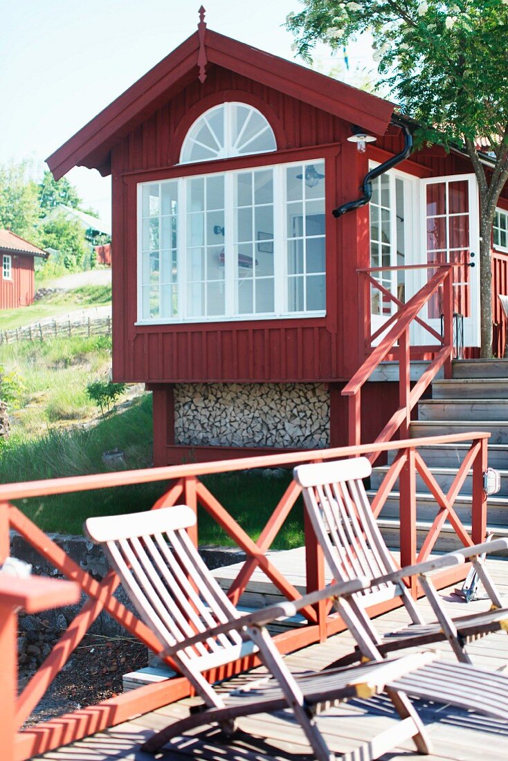 Deckchairs on wooden jetty with red railing in front of Swedish wooden house by the sea