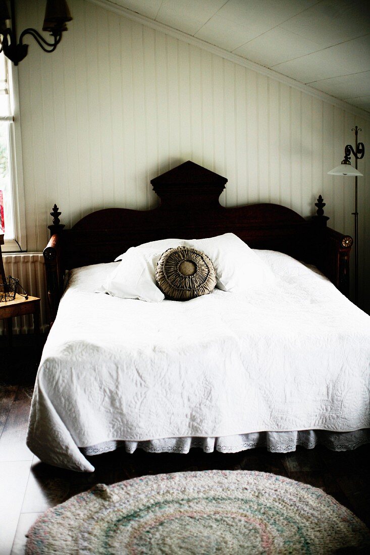 French bed with black, carved headboard and white bedspread in master bedroom in attic