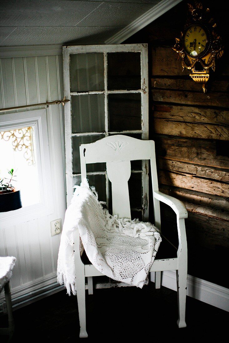 Lace blanket on white-painted chair with seat cushion in corner of wood-clad attic room