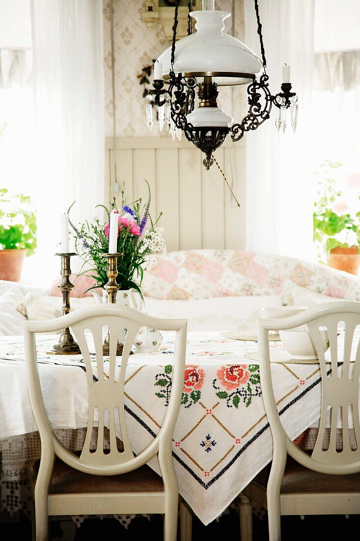 Chairs with white-painted, curved backrests at table below paraffin-lamp-style pendant lamp