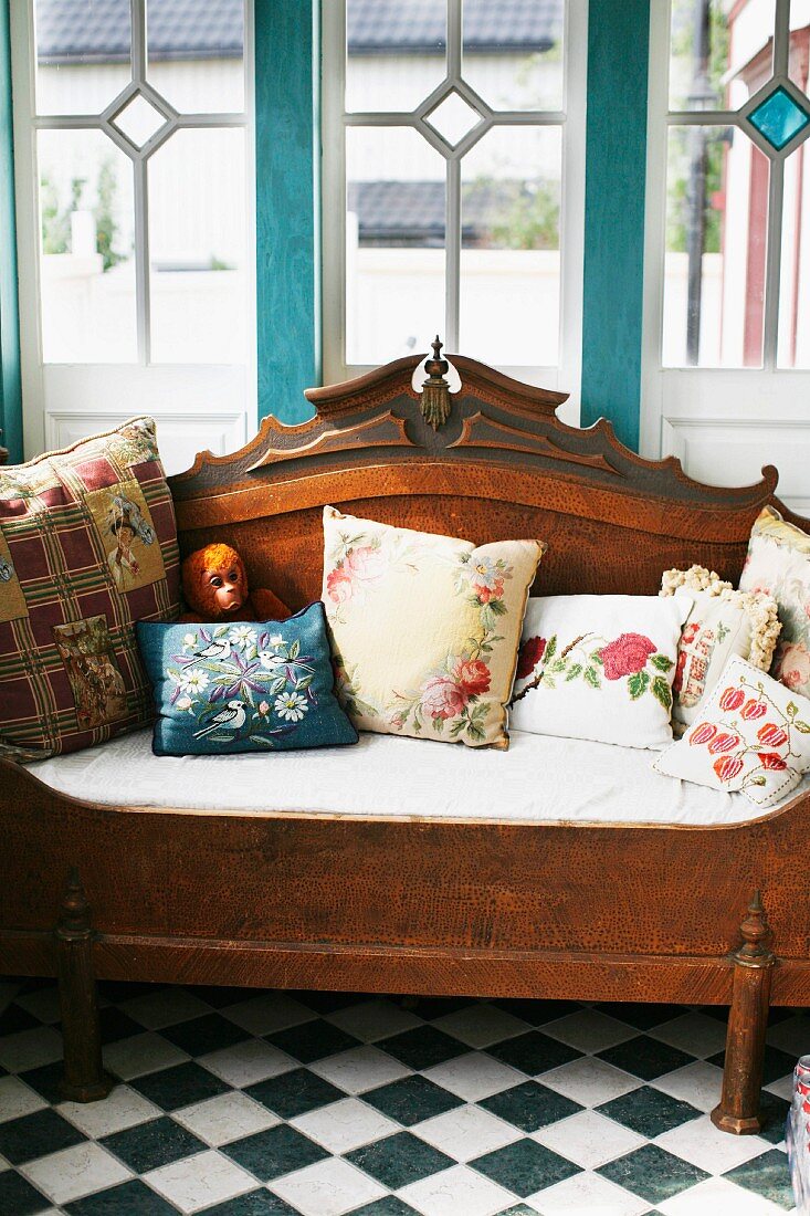 Nostalgic floral scatter cushions on antique wooden bench on chequered floor below Art Nouveau lattice windows