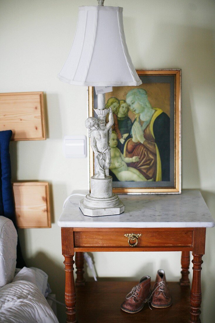 Table lamp with cherub base on wooden bedside table with marble top