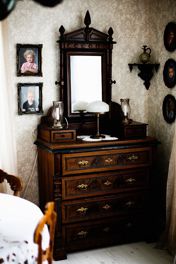 Antique chest of drawers with dresser mirror in corner surrounded by framed photos of children on walls