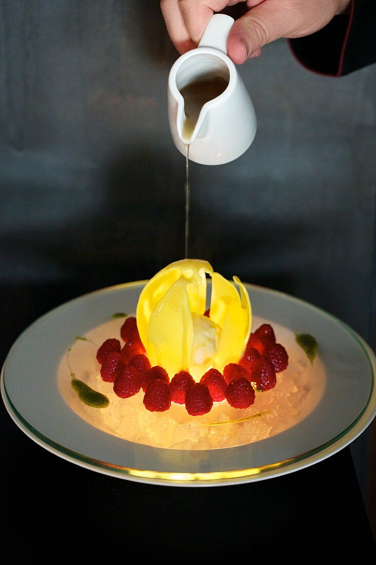 Hot Sauternes-honey sauce being drizzled over a chocolate dome on ice