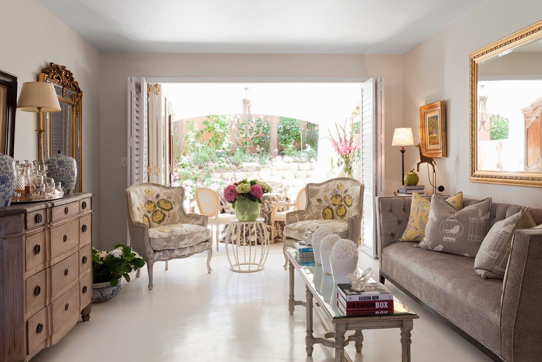 Period furniture, narrow coffee table and sofa in elegant interior with antique armchairs in front of open French windows