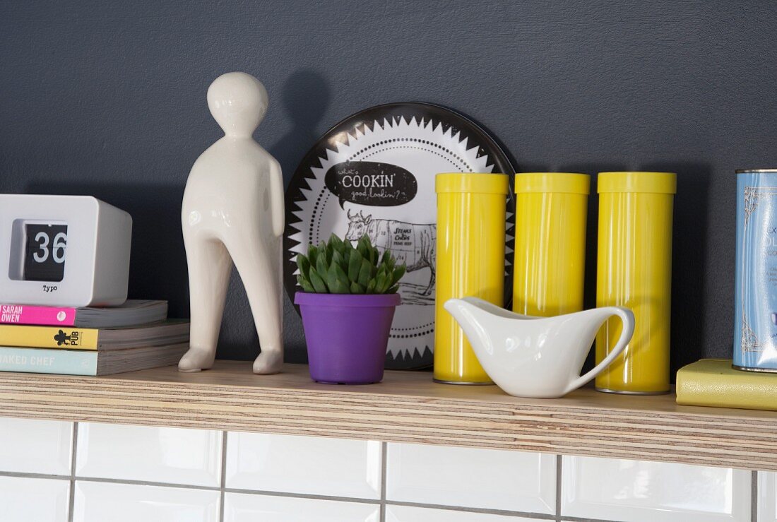 Yellow tins, purple plant pot and porcelain figurine on multiplex wooden shelf in niche