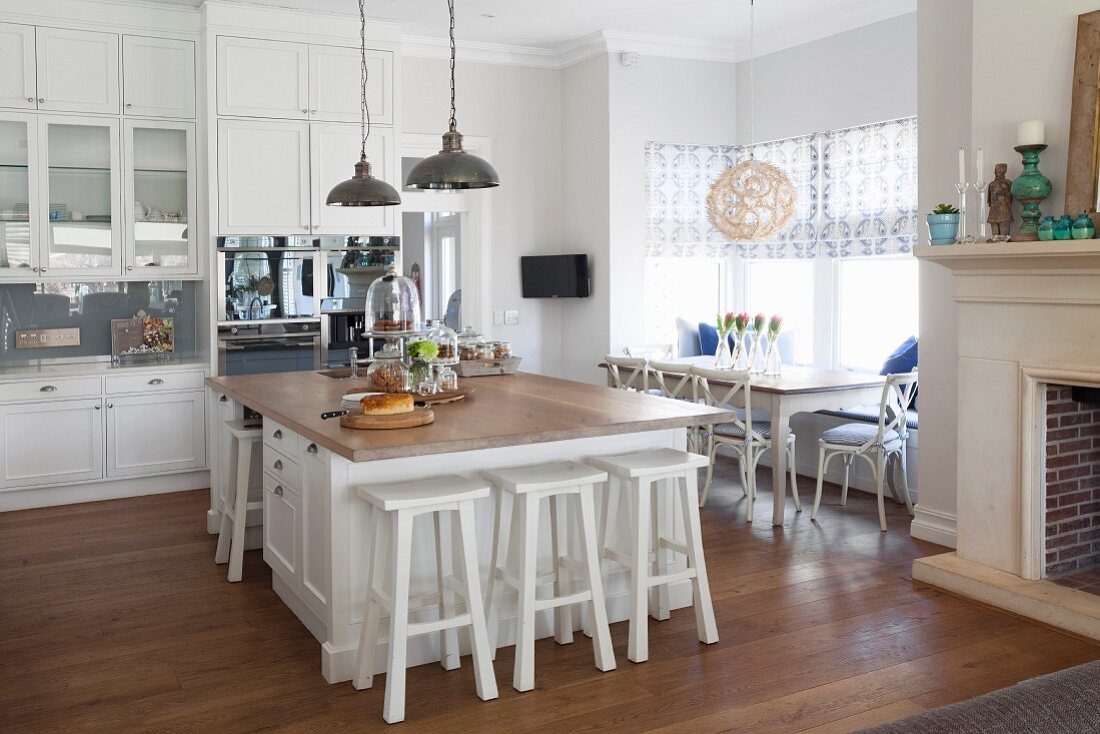 Free-standing island counter and white bar stools in open-plan, country-house kitchen with dining set below window