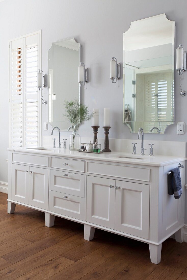 White washstand with twin sinks below two mirrors flanked by sconce lamps