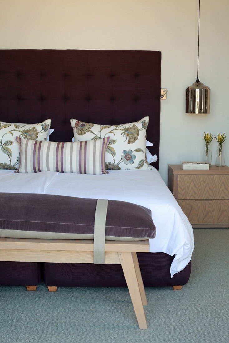 Wooden bench with seat cushion at foot of double bed with button-tufted headboard