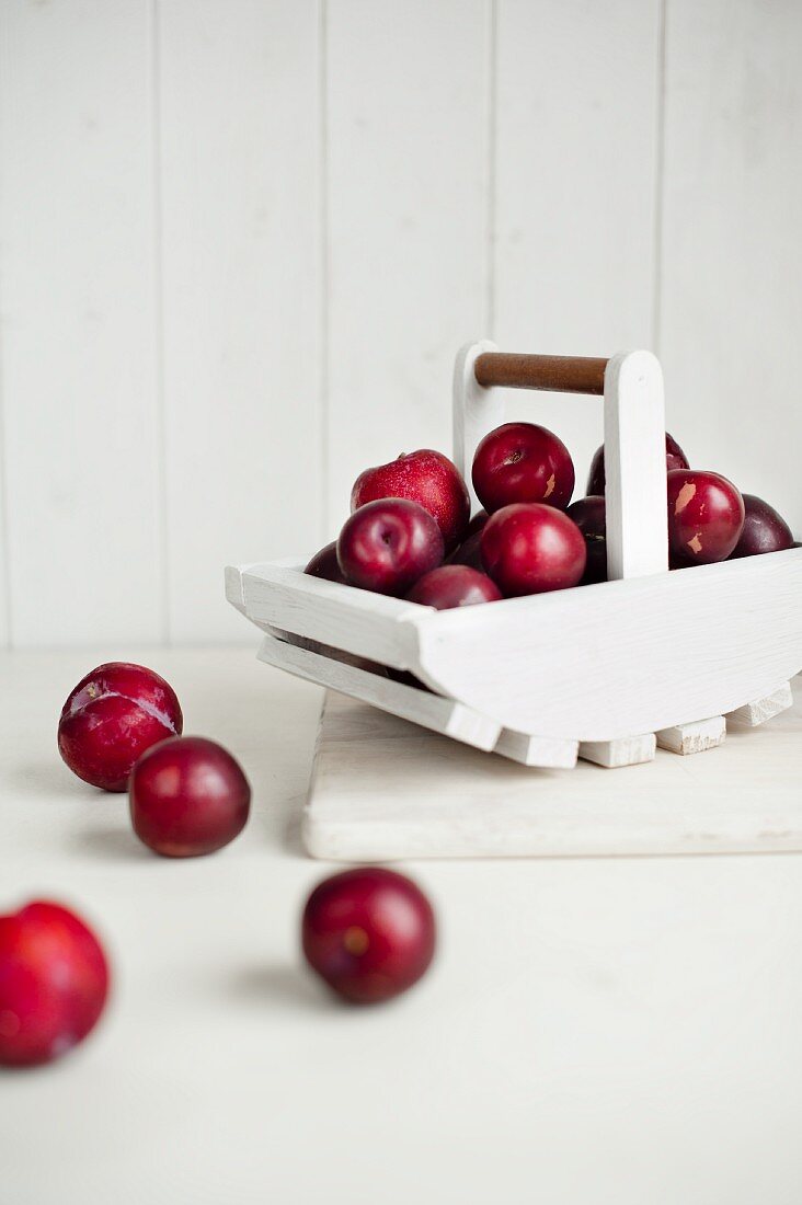 Red plums in white wooden basket and in front of it