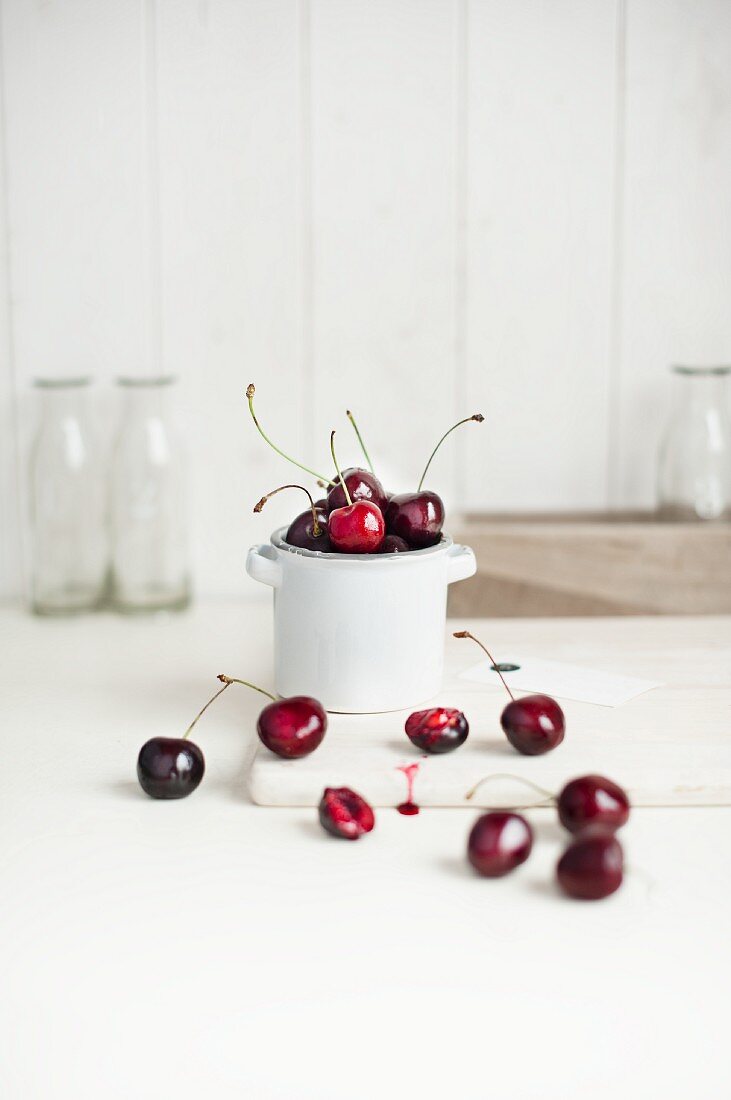 Cherries in a white porcelain pot and in front of it