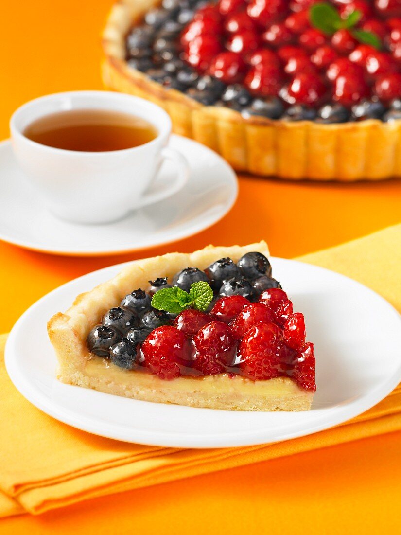 A slice of berry tart with a cup of tea