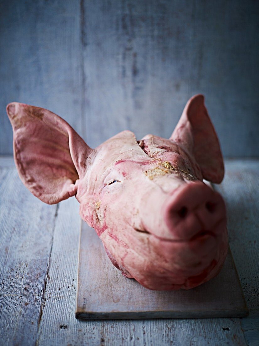 A pig's head on a chopping board against a wooden board