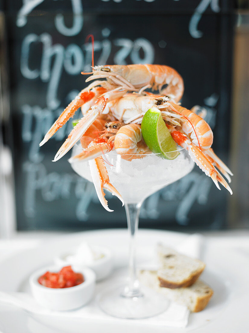 Whole scampi on ice in a cocktail glass served with lime, dips and white bread