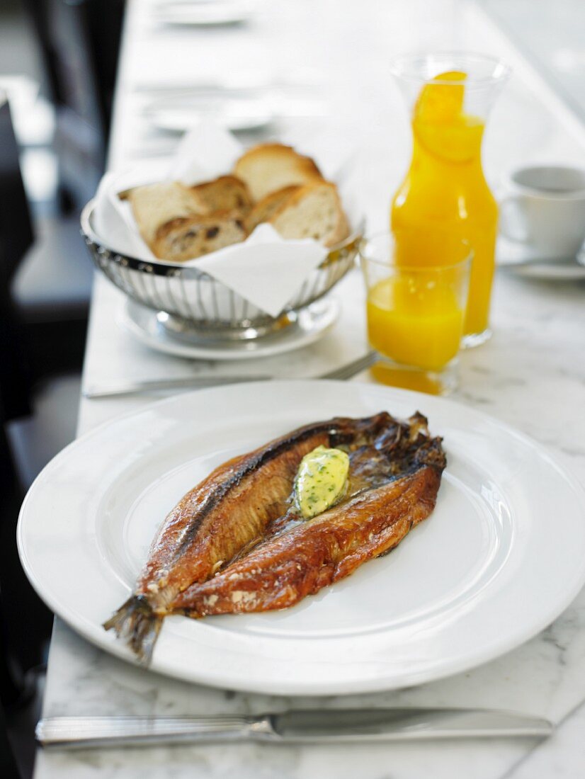 Smoked herring with herb butter with white bread and orange juice in the background