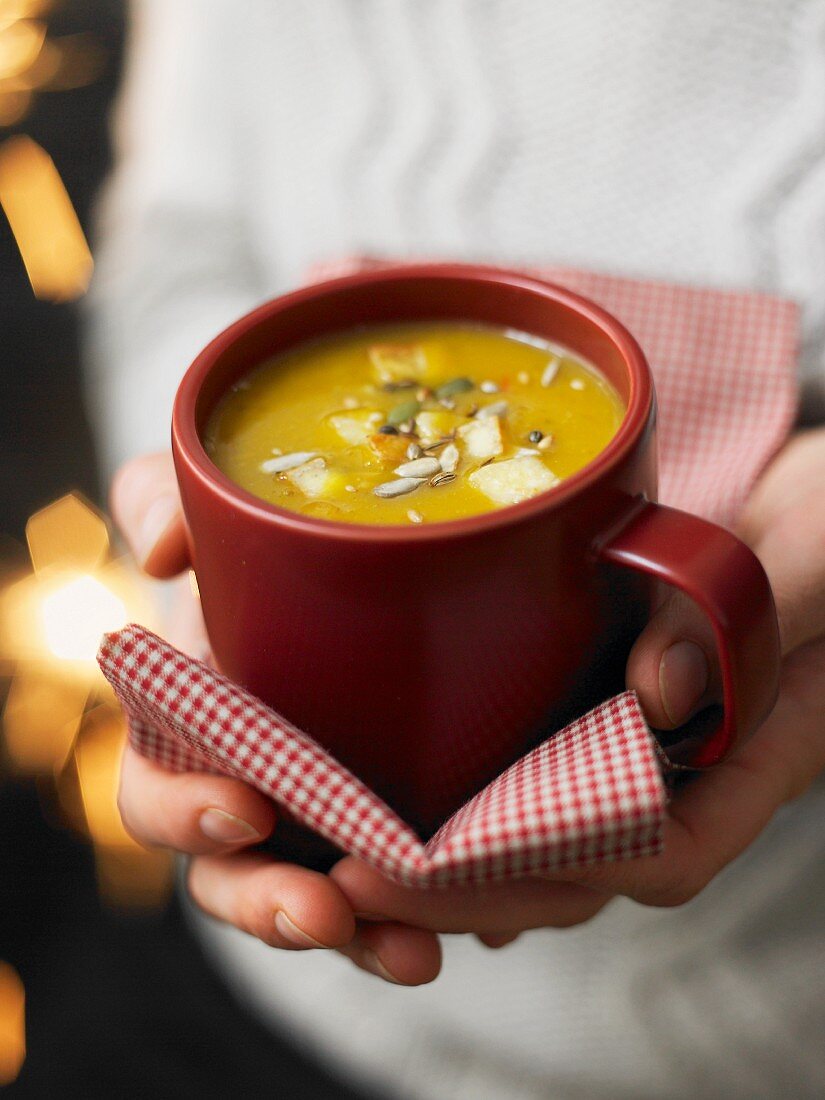 Hände halten rote Tasse mit pikanter Kürbissuppe