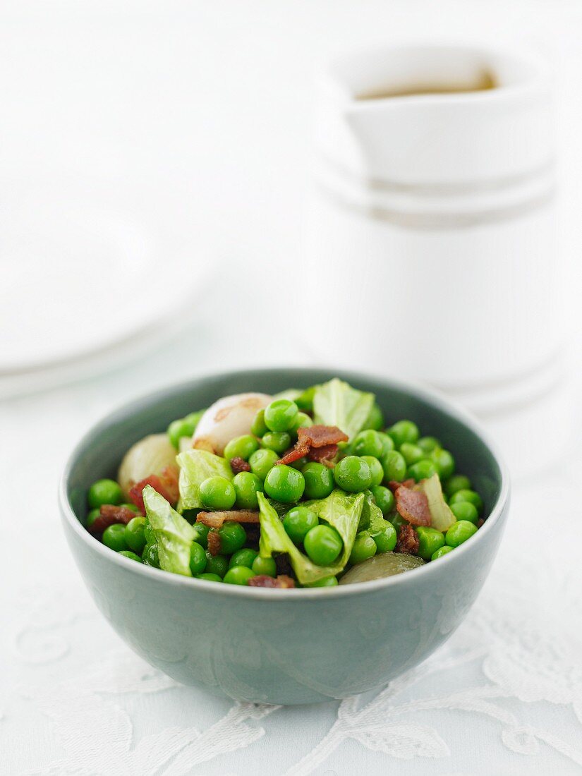 A green pea medley with bacon and shallots in a green bowl