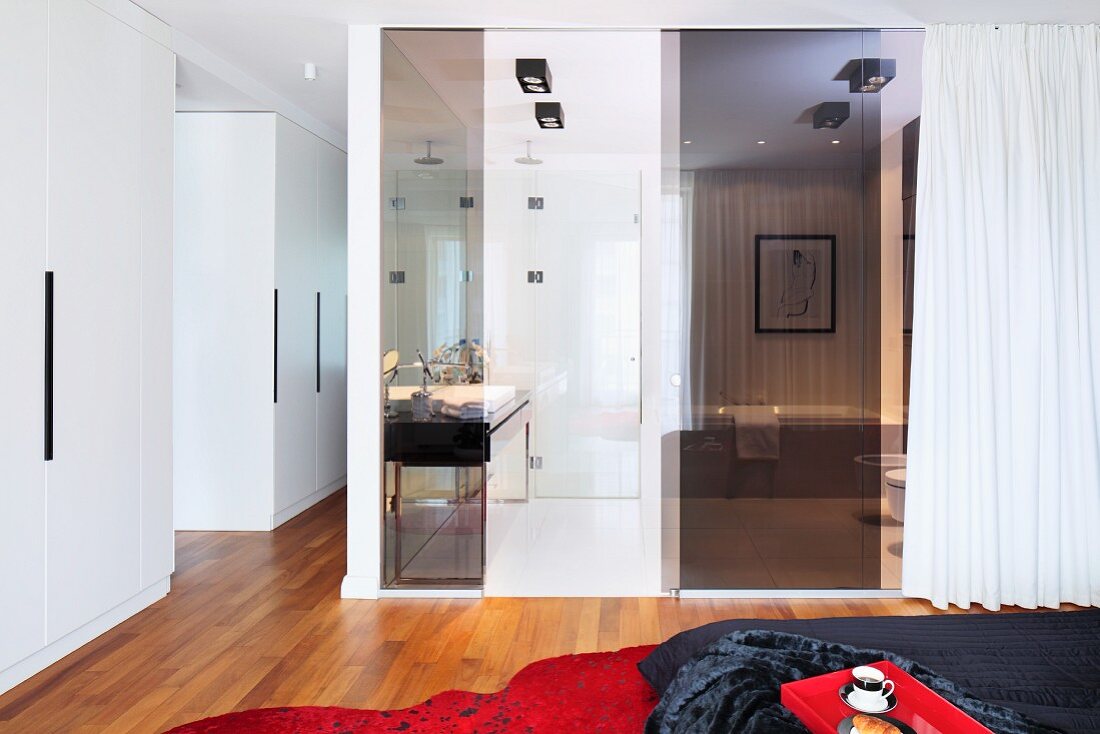 Bedroom with tinted glass panels and white curtains screening ensuite bathroom