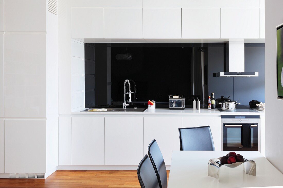 Dining area in open-plan white kitchen with black glass splashback