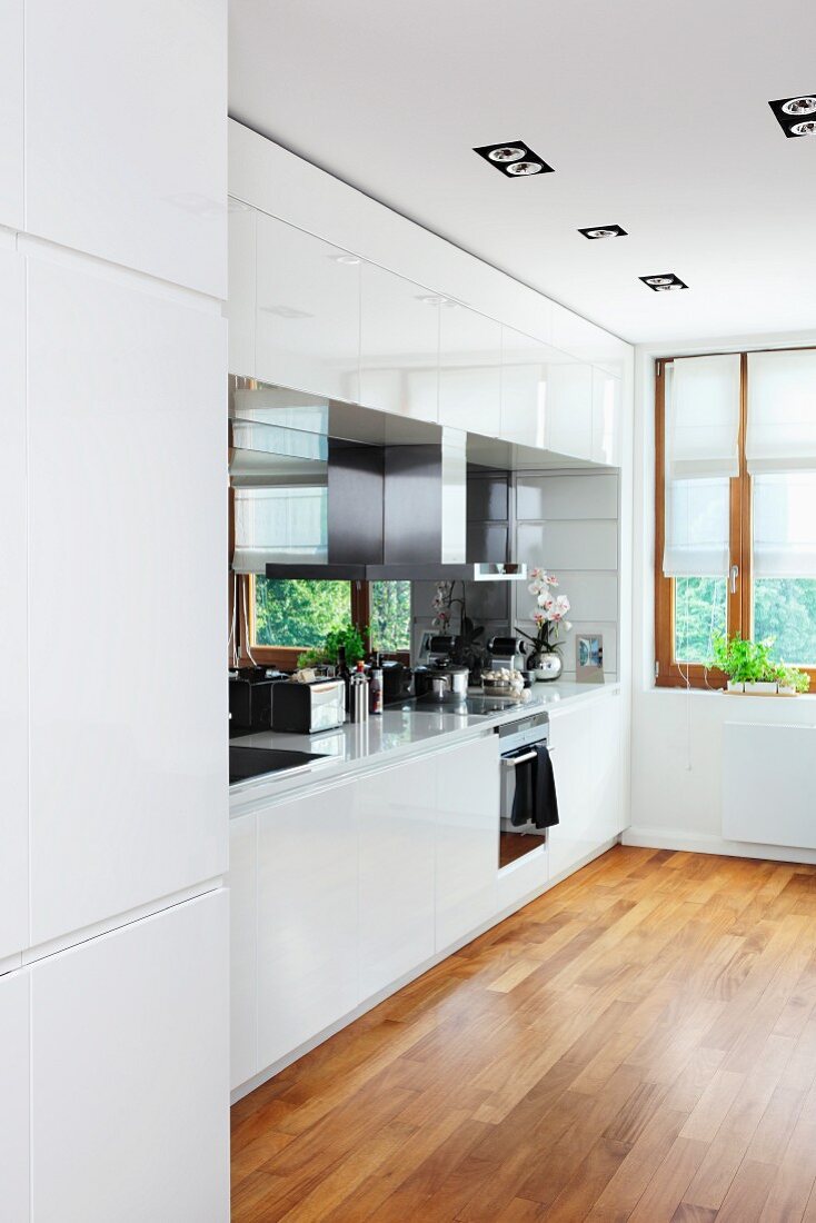 White fitted kitchen with parquet floor in modern interior with cardan lights integrated into ceiling