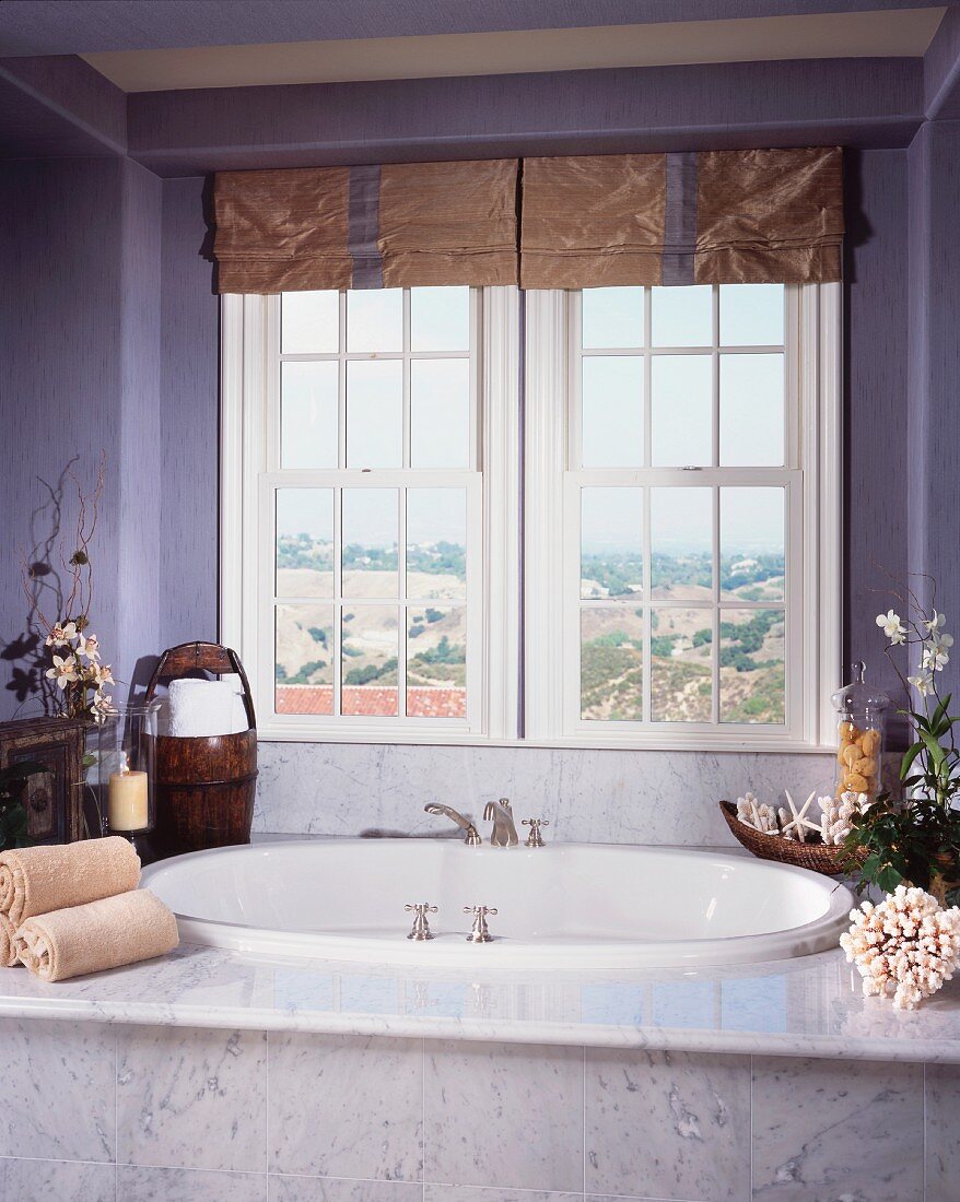 Baden mit Ausblick - vor Fenster eingebaute Badewanne mit Marmoreinfassung, auf Ablage Blumengestecke und Handtücher