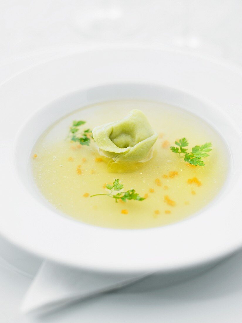 A clear broth garnished with a tortellino and chervil